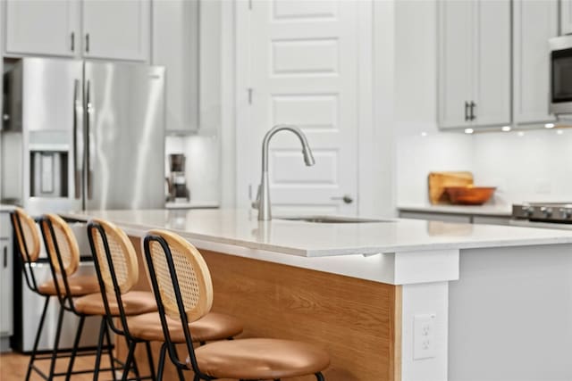 kitchen featuring a sink, stainless steel appliances, a kitchen breakfast bar, light stone countertops, and an island with sink
