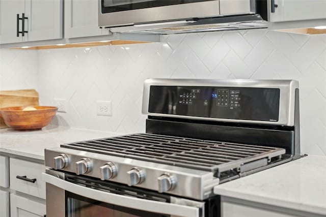 kitchen view of stainless steel gas range, decorative backsplash, and light stone counters