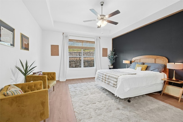 bedroom with wood finished floors, a raised ceiling, and a ceiling fan