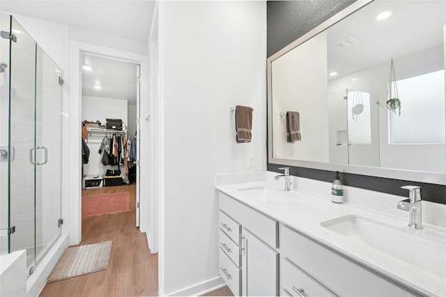 bathroom with wood finished floors, a stall shower, a spacious closet, and double vanity