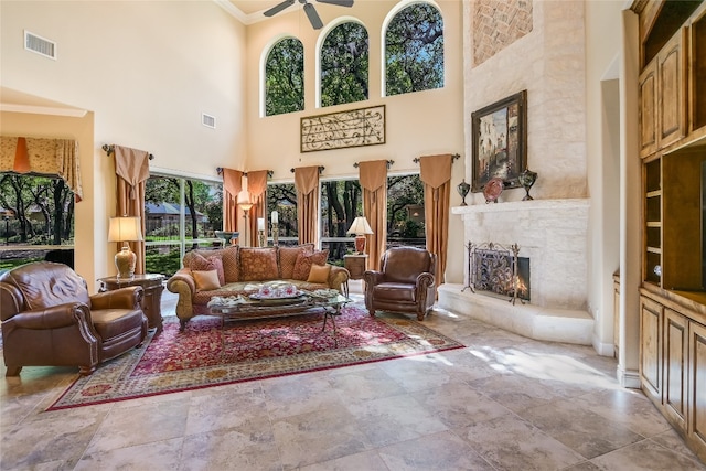 living area with a lit fireplace, a towering ceiling, a ceiling fan, stone finish flooring, and ornamental molding