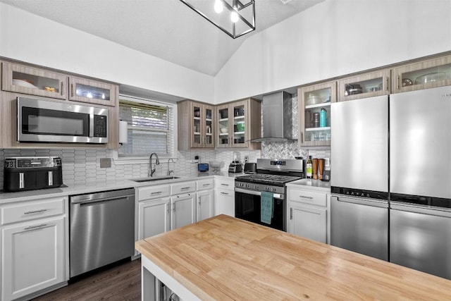 kitchen featuring stainless steel appliances, wall chimney range hood, a sink, lofted ceiling, and tasteful backsplash