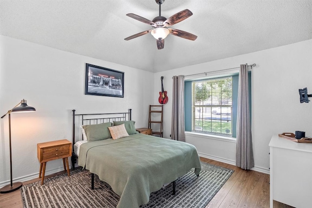 bedroom featuring light wood-type flooring, baseboards, vaulted ceiling, a textured ceiling, and ceiling fan