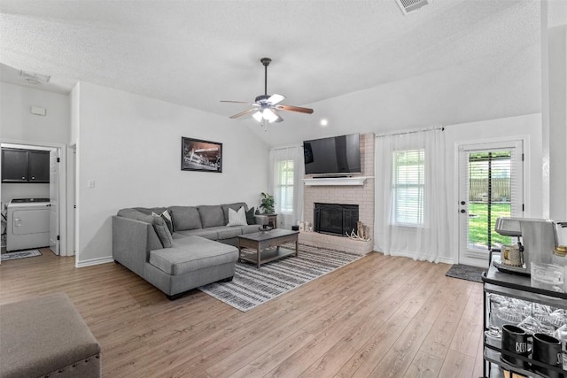 living room with washer / dryer, light wood-type flooring, a ceiling fan, lofted ceiling, and a brick fireplace