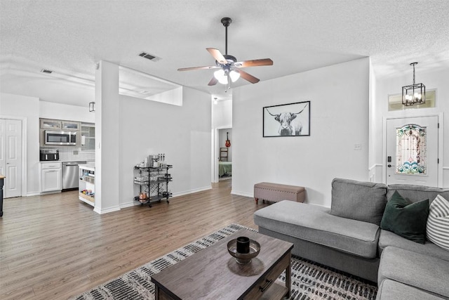 living room featuring a textured ceiling, light wood-type flooring, a ceiling fan, a chandelier, and baseboards