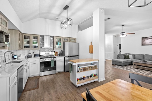 kitchen with wall chimney exhaust hood, appliances with stainless steel finishes, a sink, vaulted ceiling, and tasteful backsplash