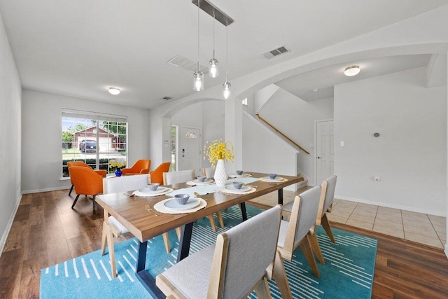 dining room featuring arched walkways, wood finished floors, baseboards, and stairs
