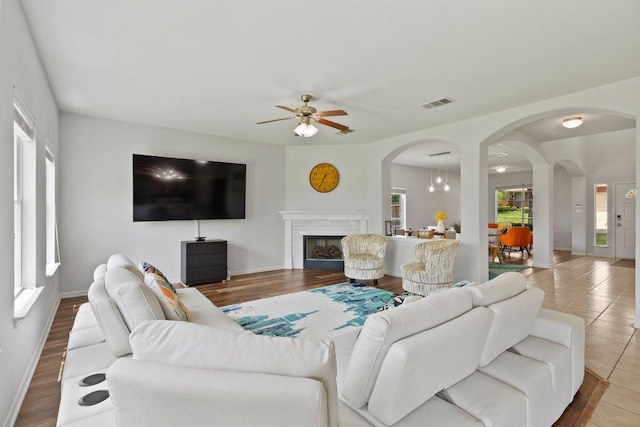 living room featuring ceiling fan, arched walkways, baseboards, and a fireplace