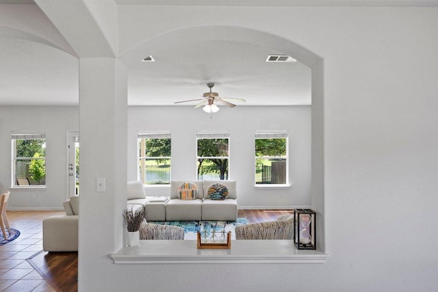 tiled living area featuring a ceiling fan, plenty of natural light, arched walkways, and baseboards
