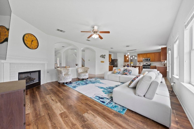 living area with ceiling fan, a brick fireplace, wood finished floors, and baseboards