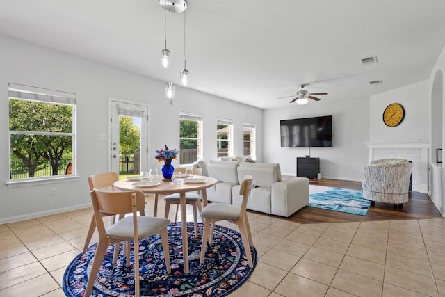dining space featuring light tile patterned flooring, a ceiling fan, baseboards, and a fireplace