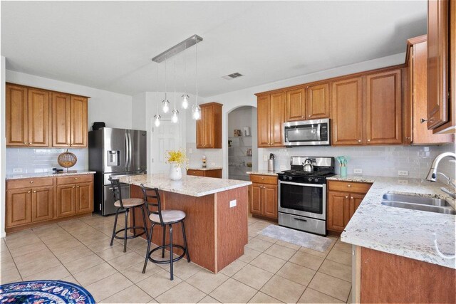 kitchen with stainless steel appliances, a sink, backsplash, brown cabinets, and light tile patterned floors