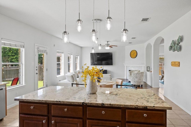 kitchen featuring light tile patterned floors, arched walkways, a ceiling fan, light stone countertops, and decorative light fixtures