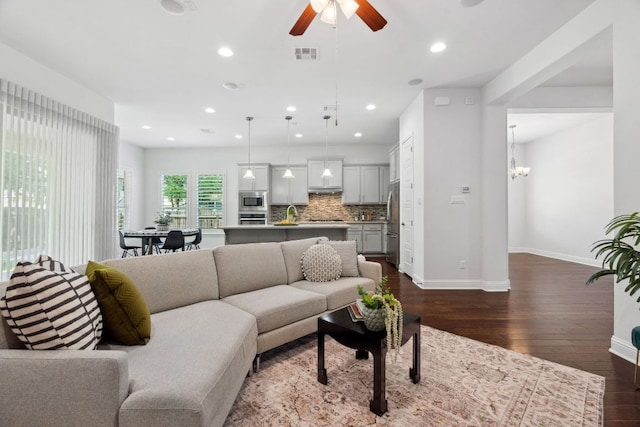 living area featuring dark wood-type flooring, baseboards, ceiling fan, recessed lighting, and a chandelier