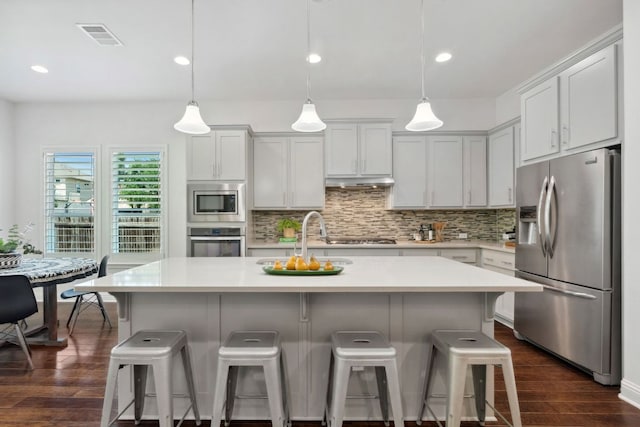 kitchen featuring appliances with stainless steel finishes, dark wood-style flooring, tasteful backsplash, light countertops, and a breakfast bar