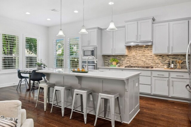 kitchen with light countertops, stainless steel appliances, backsplash, a breakfast bar, and dark wood-style floors