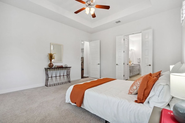 bedroom with carpet flooring, a tray ceiling, baseboards, and ensuite bath
