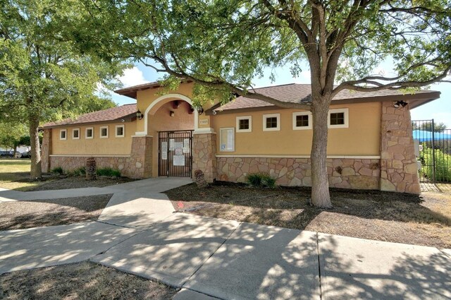 view of front facade with a gate, stucco siding, stone siding, and fence