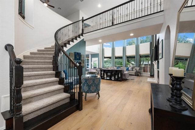 staircase with wood finished floors, a towering ceiling, plenty of natural light, and ceiling fan