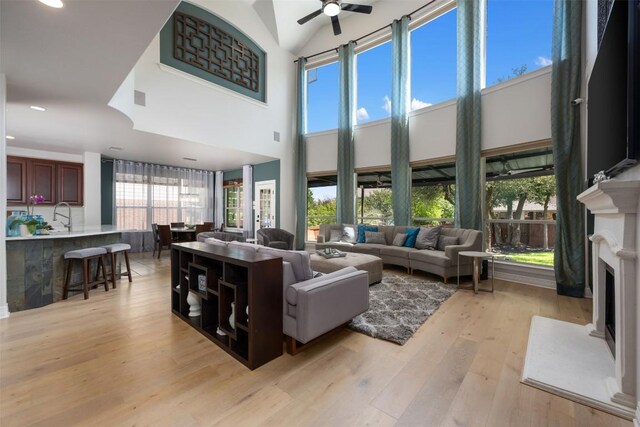living room featuring a fireplace, recessed lighting, ceiling fan, light wood-style flooring, and high vaulted ceiling