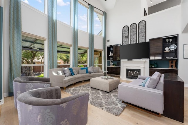 living room with a towering ceiling, plenty of natural light, wood finished floors, and a glass covered fireplace
