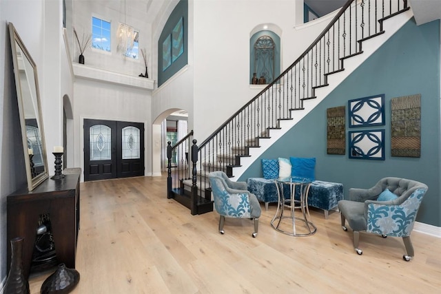 entrance foyer with arched walkways, a high ceiling, french doors, stairs, and wood finished floors