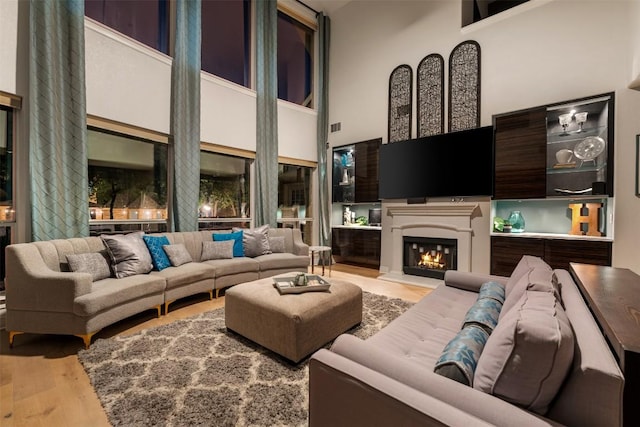 living area with wood finished floors, a towering ceiling, and a warm lit fireplace