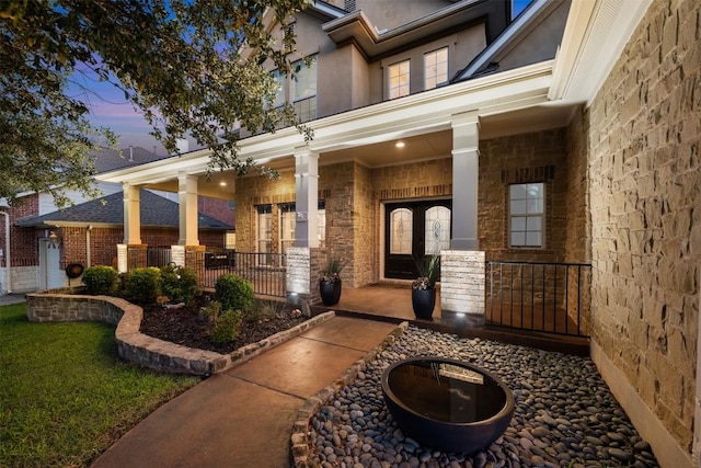 view of exterior entry featuring a porch, stone siding, and french doors