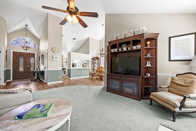 living area featuring a chandelier, high vaulted ceiling, carpet, baseboards, and a ceiling fan