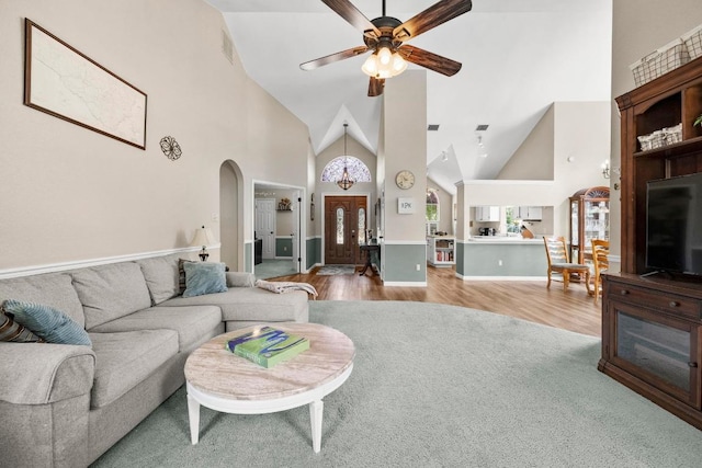 living area featuring high vaulted ceiling, ceiling fan, wood finished floors, arched walkways, and baseboards