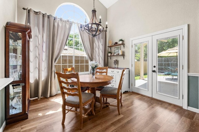 dining space featuring wood finished floors, french doors, a chandelier, healthy amount of natural light, and vaulted ceiling