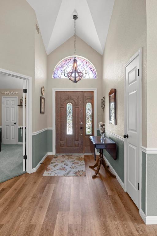 foyer featuring a chandelier, high vaulted ceiling, wood finished floors, and baseboards