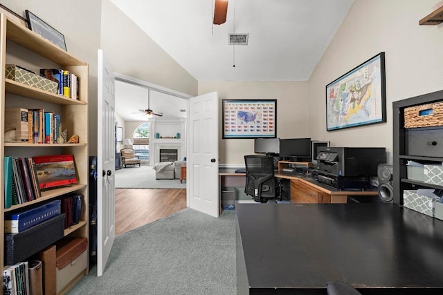 home office with a ceiling fan, lofted ceiling, a glass covered fireplace, and carpet