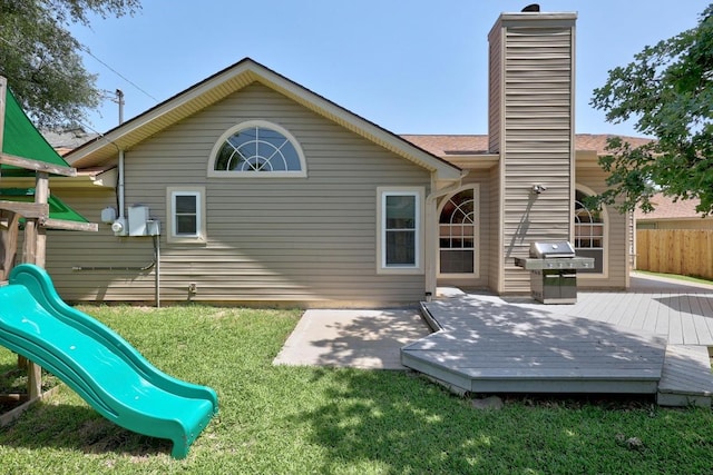 rear view of property featuring a playground, a wooden deck, and a chimney