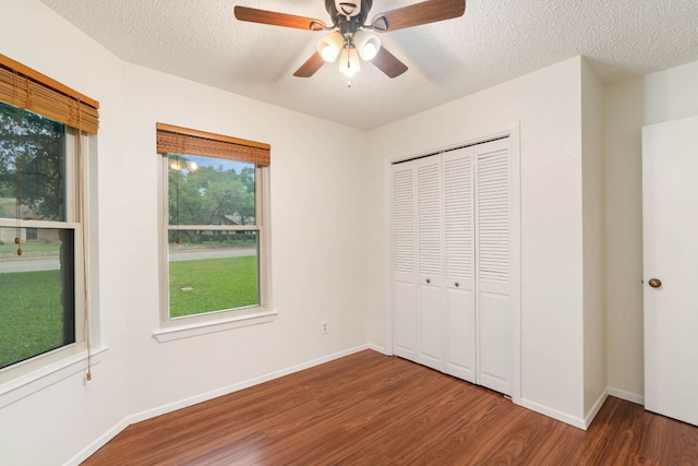 unfurnished bedroom featuring dark wood-style flooring, a closet, a textured ceiling, baseboards, and ceiling fan