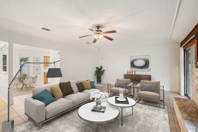 living room with light tile patterned flooring, a ceiling fan, and a textured ceiling
