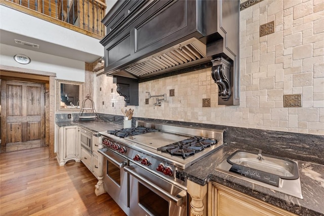 kitchen with stainless steel appliances, backsplash, light wood-style flooring, and dark stone counters