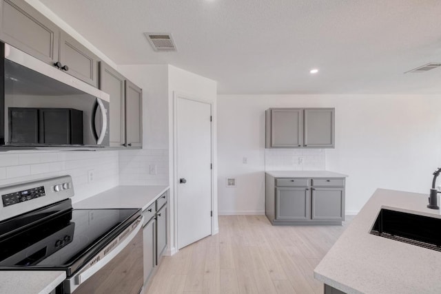 303 Flinn St, Hutto, TX 78634 - kitchen with stainless steel appliances, gray cabinets, light wood-style flooring, light countertops, and backsplash