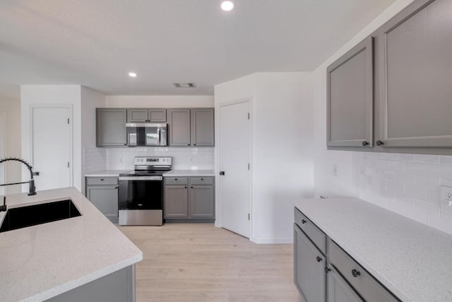 303 Flinn St, Hutto, TX 78634 - kitchen featuring appliances with stainless steel finishes, a sink, gray cabinetry, tasteful backsplash, and recessed lighting