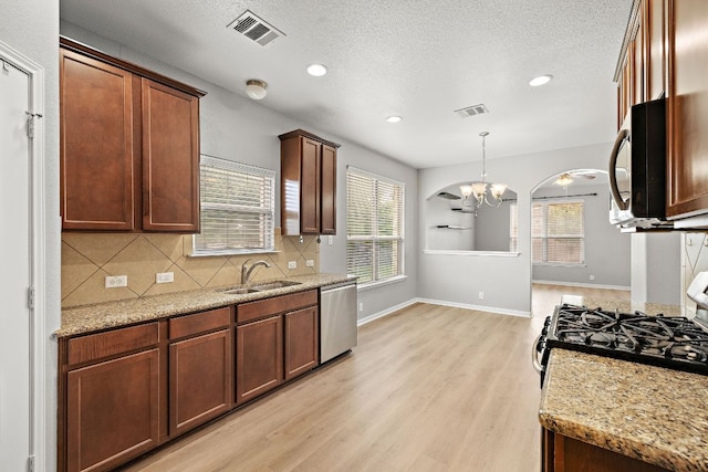 kitchen featuring appliances with stainless steel finishes, a sink, light wood-style floors, backsplash, and a chandelier