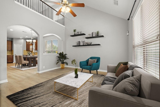 living area featuring arched walkways, high vaulted ceiling, ceiling fan, light wood-style floors, and a chandelier