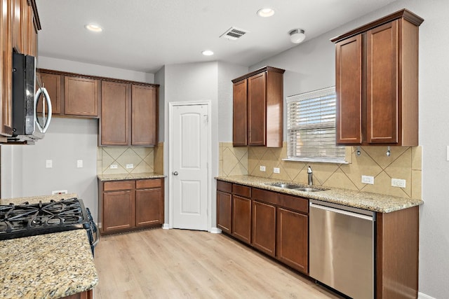 kitchen featuring a sink, appliances with stainless steel finishes, light wood finished floors, light stone countertops, and backsplash