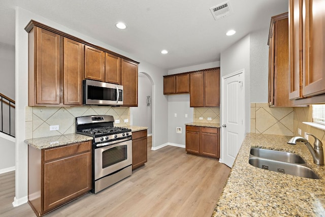 kitchen featuring appliances with stainless steel finishes, a sink, light wood-type flooring, arched walkways, and recessed lighting