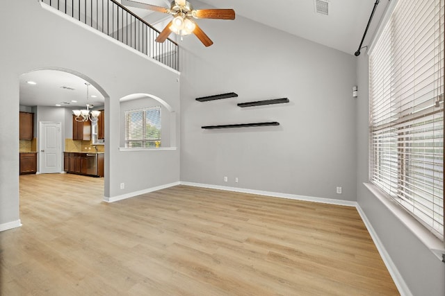 unfurnished living room with a towering ceiling, a ceiling fan, a chandelier, baseboards, and light wood-style flooring