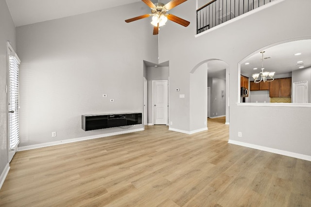 unfurnished living room featuring ceiling fan, arched walkways, a chandelier, a towering ceiling, and baseboards
