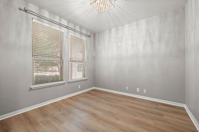 empty room featuring wood finished floors, a chandelier, and baseboards