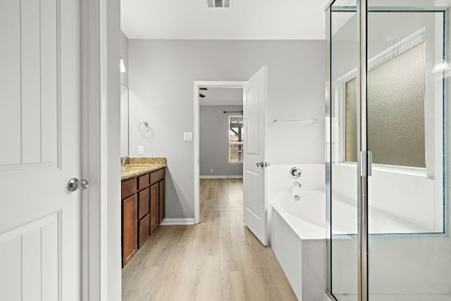 bathroom featuring wood finished floors, vanity, a bath, a shower stall, and baseboards