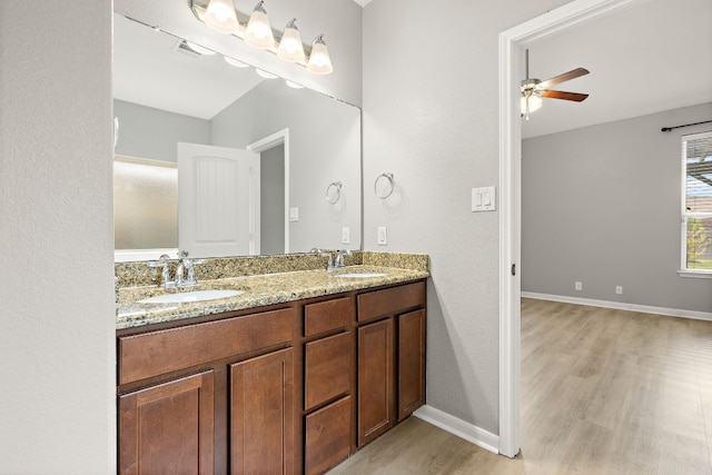 full bath featuring wood finished floors, double vanity, a ceiling fan, and baseboards