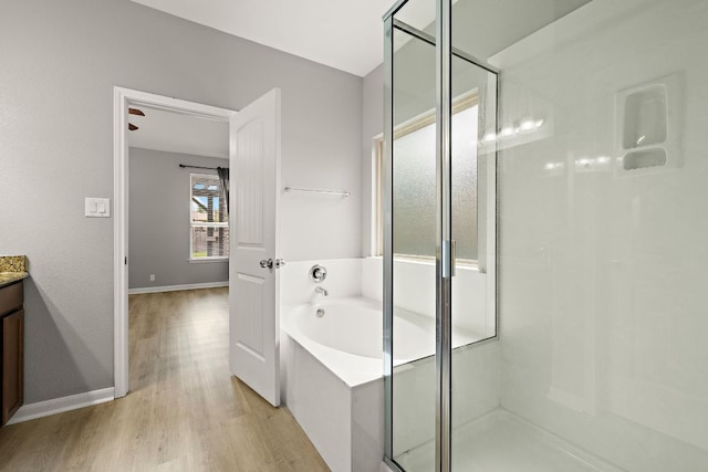 full bathroom featuring wood finished floors, a shower stall, a bath, vanity, and baseboards