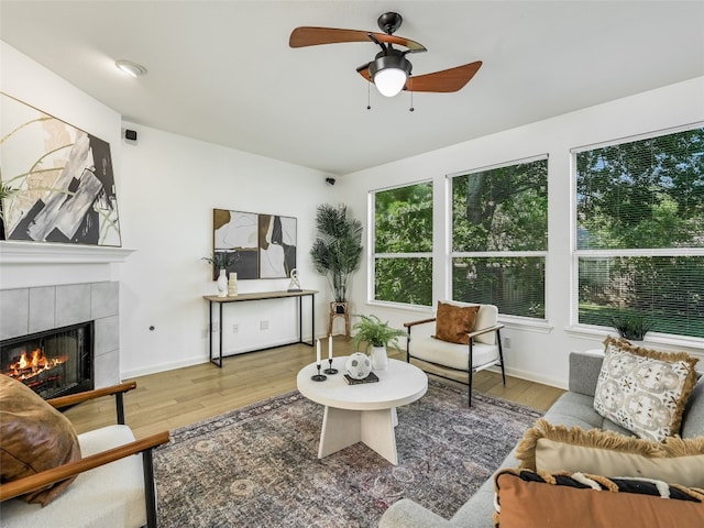 living area with a tiled fireplace, wood finished floors, ceiling fan, and baseboards